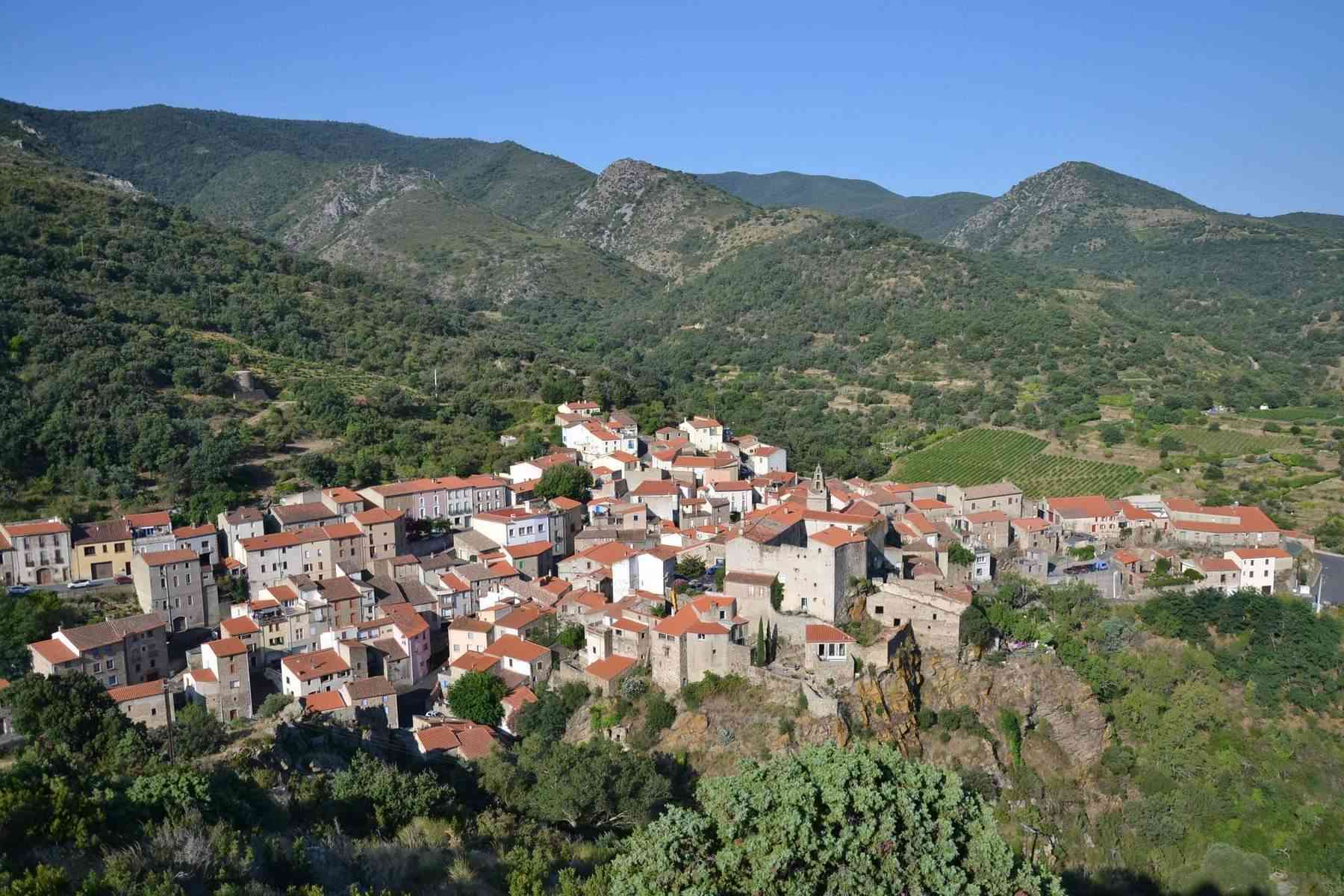 Caramany sur son socle rocheux, ses maisons aux toits de tuiles et les collines environnantes
